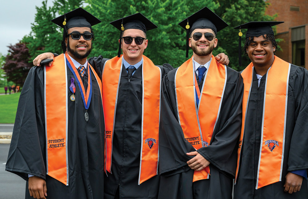 four Bucknell graduates wearing orange academic stoles