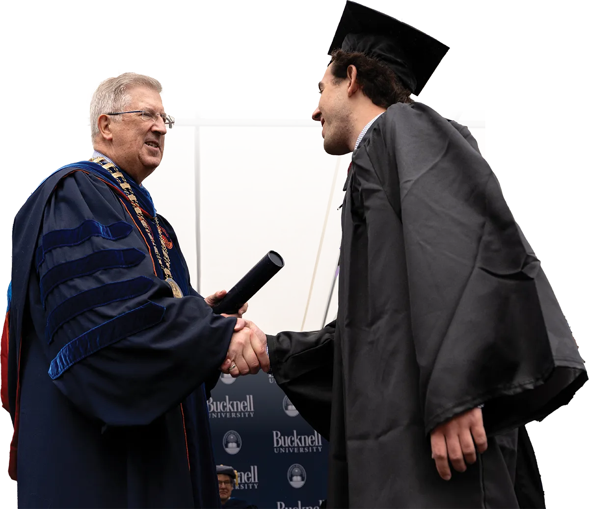 student shaking the hand of a faculty member as he receives his degree on stage at a graduation ceremony