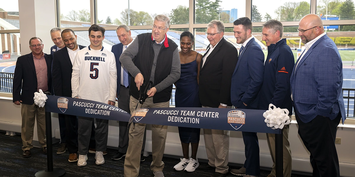 President John Bravman standing with a group of athletics staff and students while cutting a ribbon that reads "Pascucci Team Center Dedication"