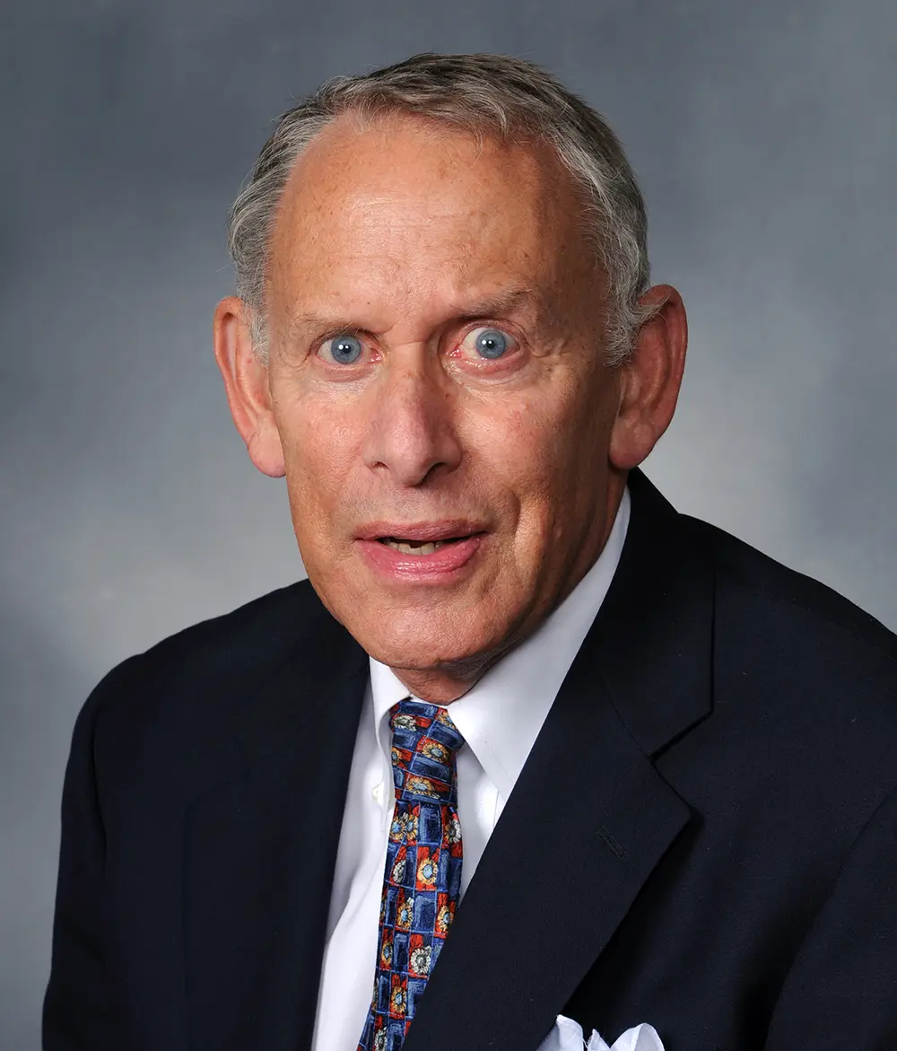 Portrait headshot close-up photo view of Stuart Berelson smiling in a dark navy blue business suit with a white button-up dress shirt underneath and a multi-colored (blue, red, yellow) tie equipped showing a floral design pattern mimicked all over the tie