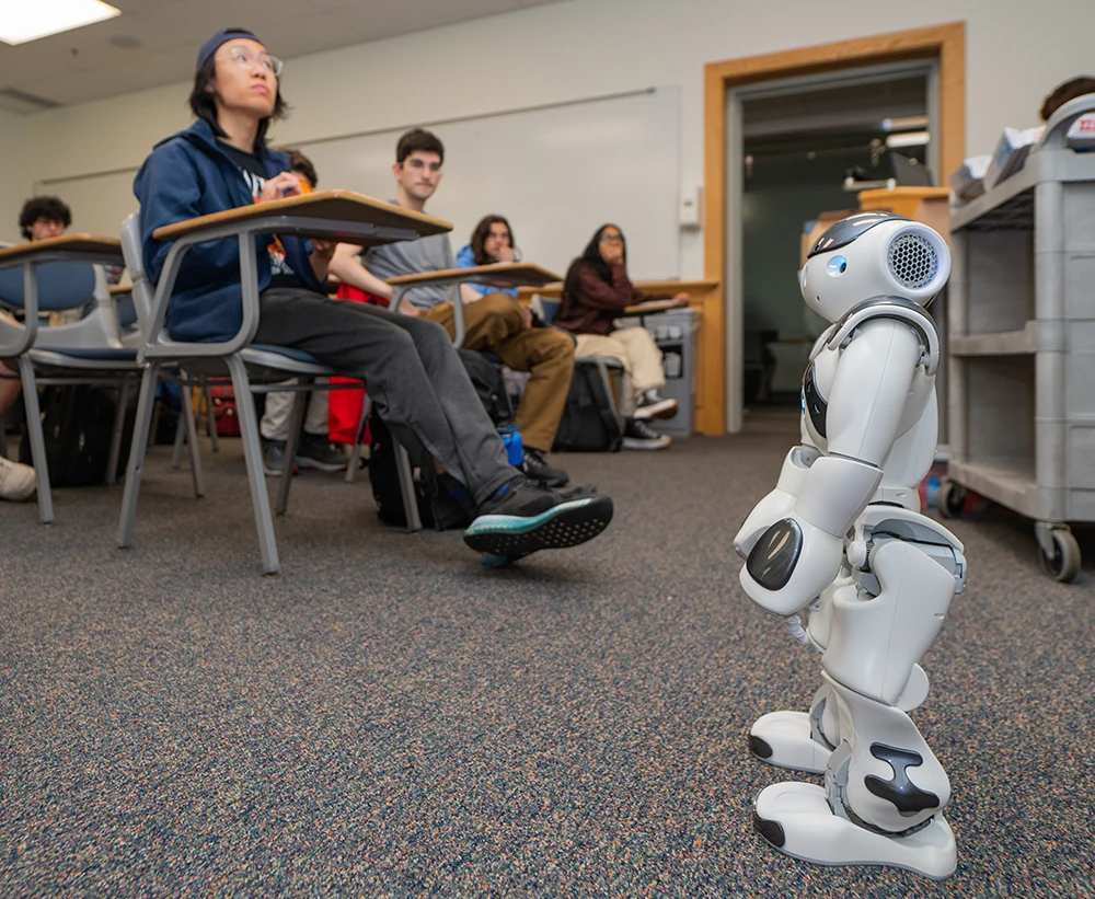 View of classroom with a small robot positioned in front of students seated at their desks