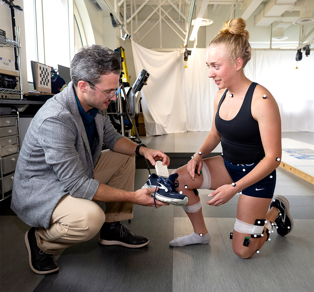 man and woman kneeling on ground talking while the man inserts an adjustable wedge into the woman's shoe