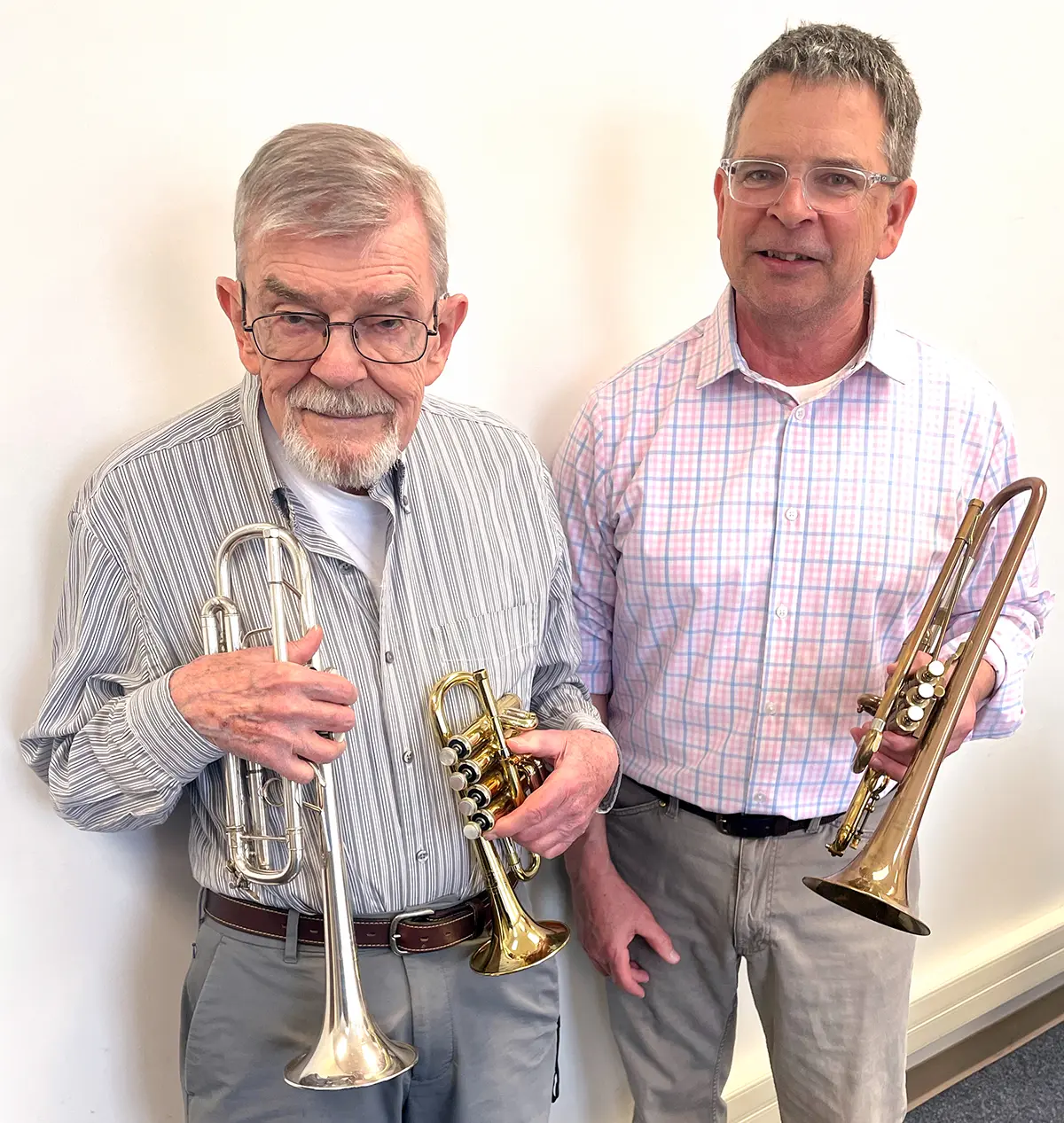 Portrait indoor photograph of Richard Berggren ’57 (left) presenting three special trumpets to Professor William Kenny, music, at the Bucknell band’s spring concert at the Weis Center for the Performing Arts as both men smile standing next to each other
