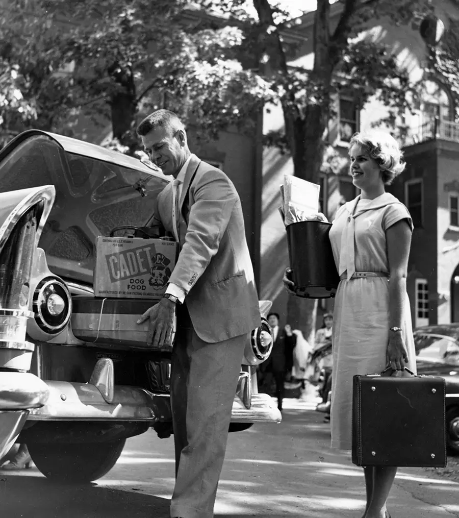 black and white photo of a man and woman loading luggage onto a car