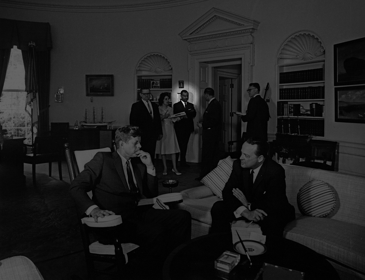 black and white photo of Sulliman standing at a door in the Oval Office during a meeting between President John F. Kennedy and the newly appointed United States Ambassador to West Germany, George McGhee