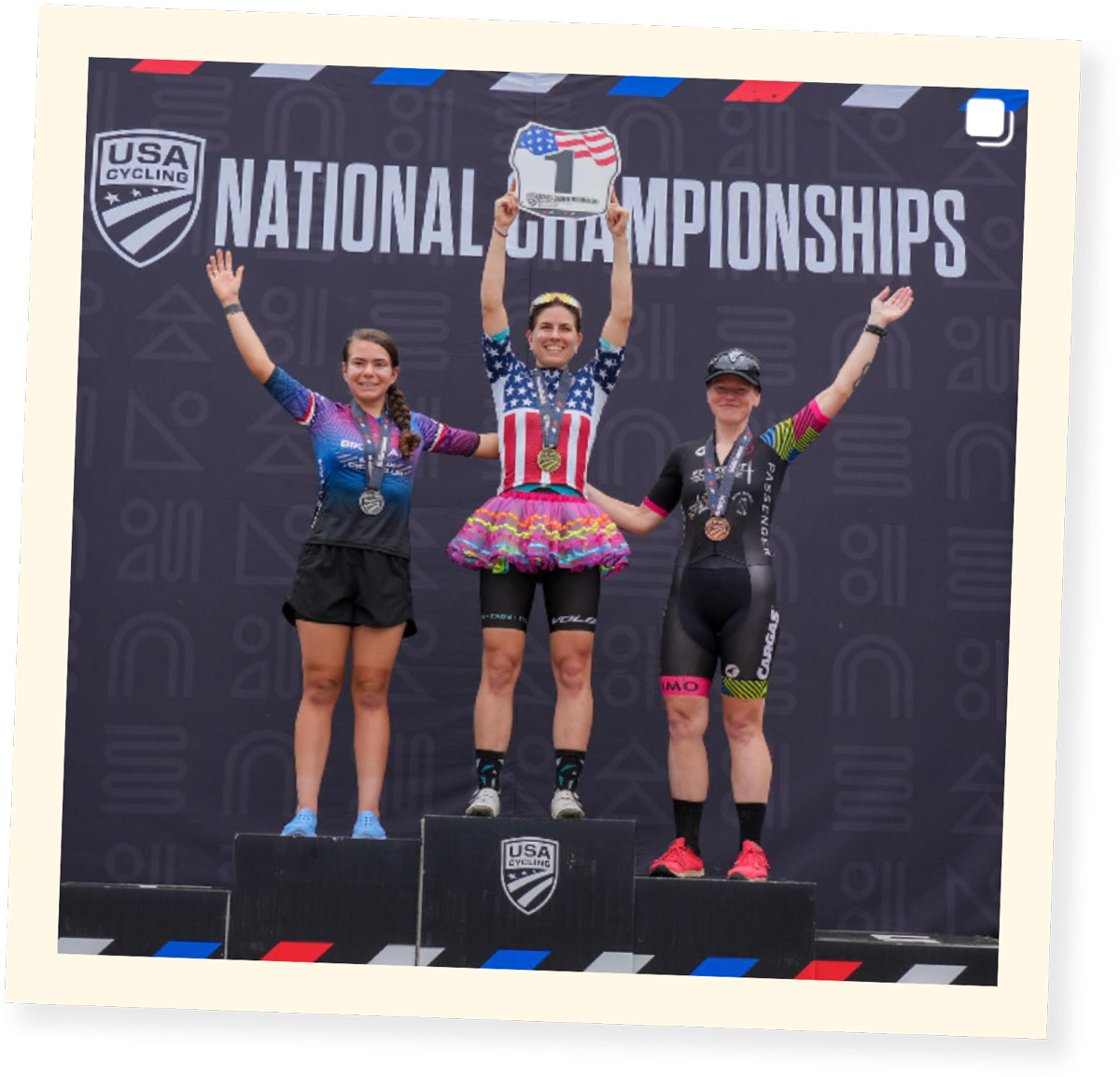 wide shot of Kelly Desharnais Catale standing atop the the 2023 National Cross-Country Mountain Bike Championships winners podium dressed in a tutu and hoisting the award over her head