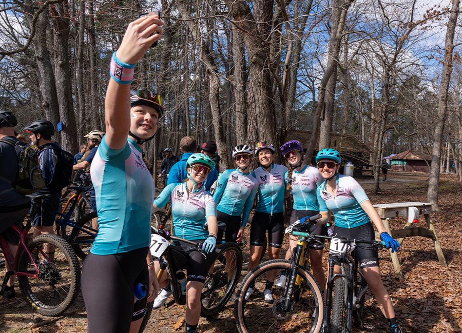 candid shot of Kelly Desharnais Catale ‘12 (center) taking a photo with members of her junior race team at a biking event