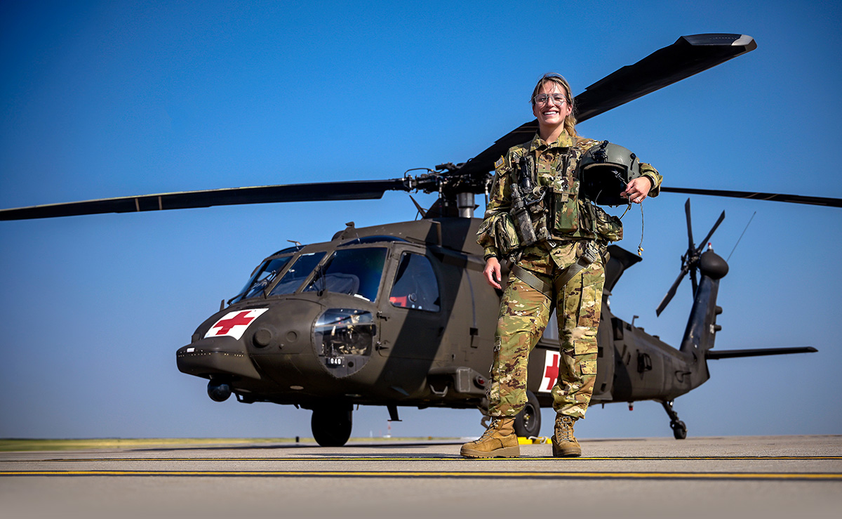 Nicole Vacas-English in camo National Guard uniform holding helmet in front of medic helicopter