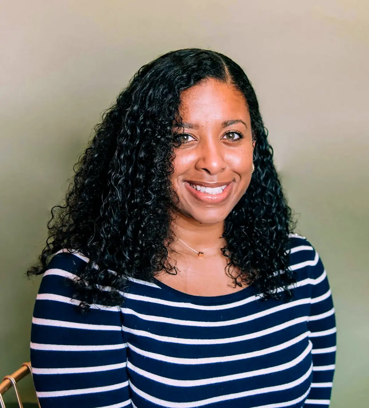 Portrait headshot photograph of Melissa Fuller Woods smiling in a dark navy blue long-sleeve v-neck shirt that contains white horizontal stripes on them