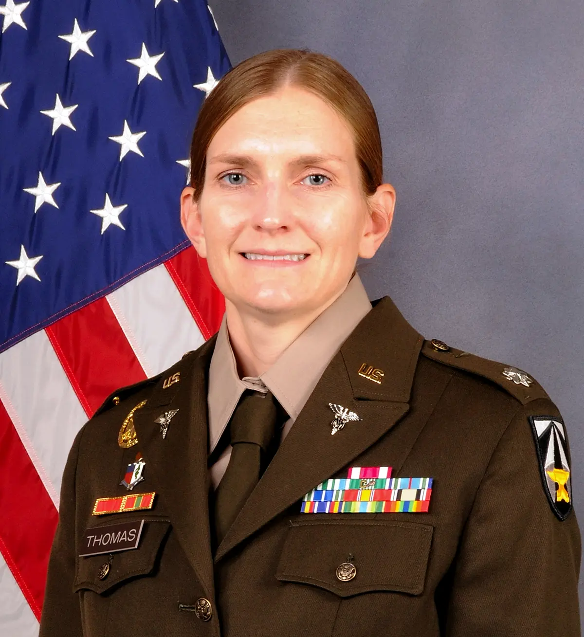Portrait headshot photograph of Connie Barko Thomas smiling in her U.S. Army military attire outfit as she stands in front of a United States of America flag background