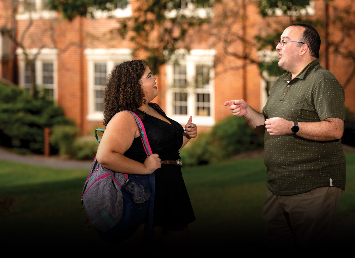 Two people talking in front of a brick building with windows.