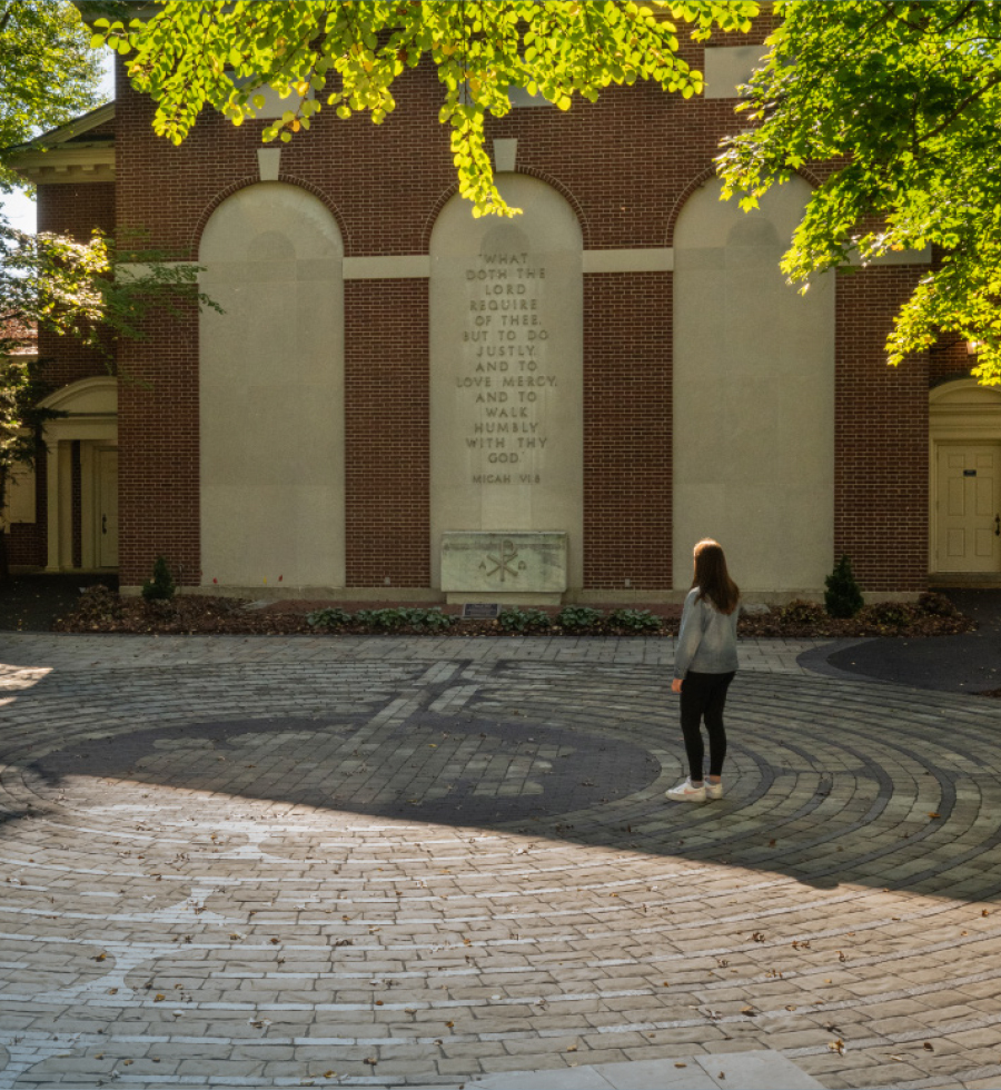 student walking through stone-inlaid labyrinth installed behind Rooke Chapel