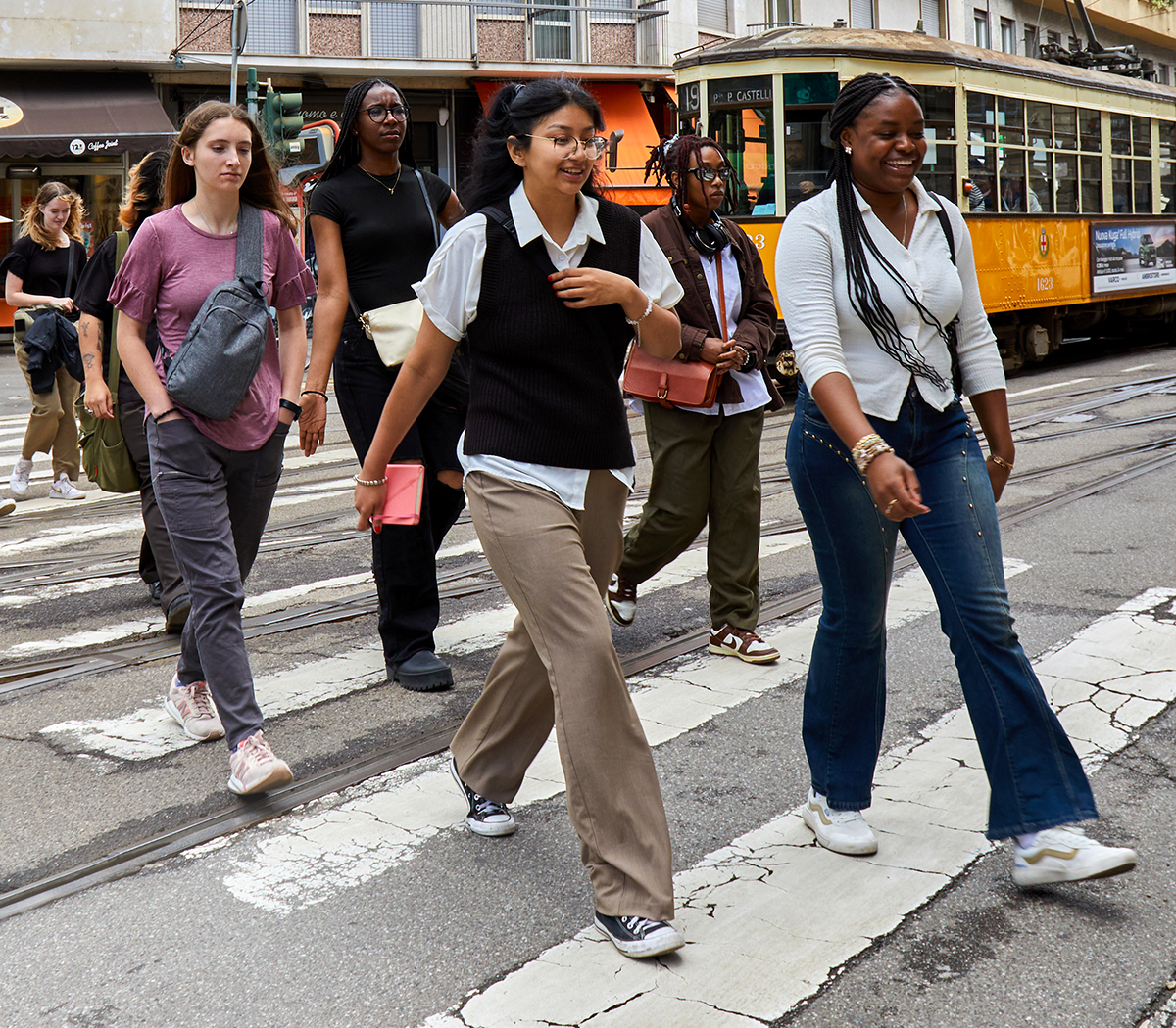 Five young adults crossing a city street, with a yellow tram and buildings in the background.