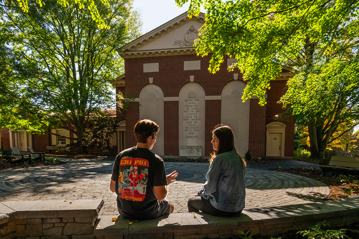 students sitting by the new stone-inlaid labyrinth flooring installed behind Rooke Chapel