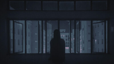 A silhouette of a person looking out of a wide window with their back turned to the viewer.