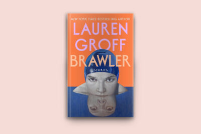 A cover of Lauren Groff’s Brawler. The book is an orange background with a swimmer's face in the front, halfway out of water. The book is against a pink background.