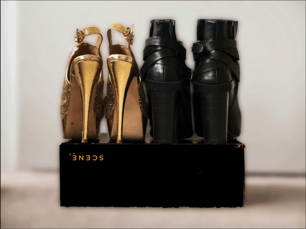 (from L-R) the backs of golden high heels next to the backs on black ankle high high heeled boots, both on top of a black box.