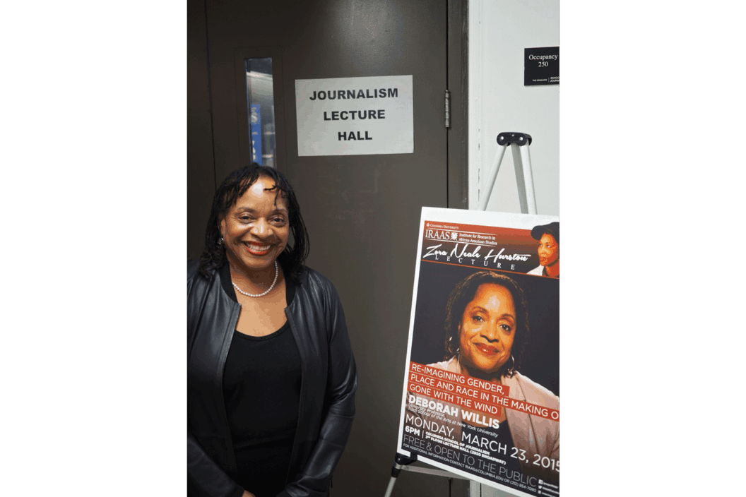Color photograph of the artist posing next to a poster for her talk.