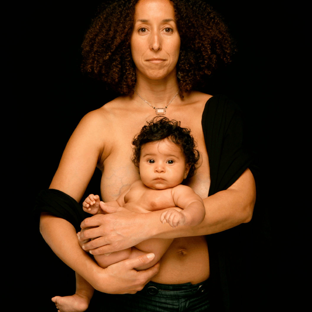 Color photograph of a nude woman holding her child to her chest.