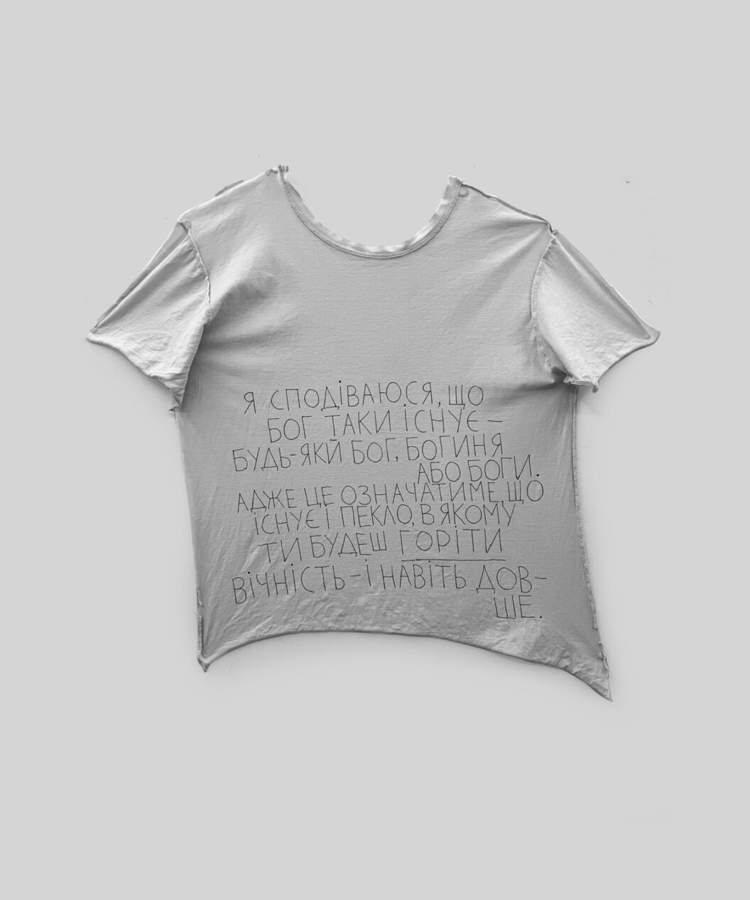 A photograph of a poem-prayer written in black ink on a plain white t-shirt.