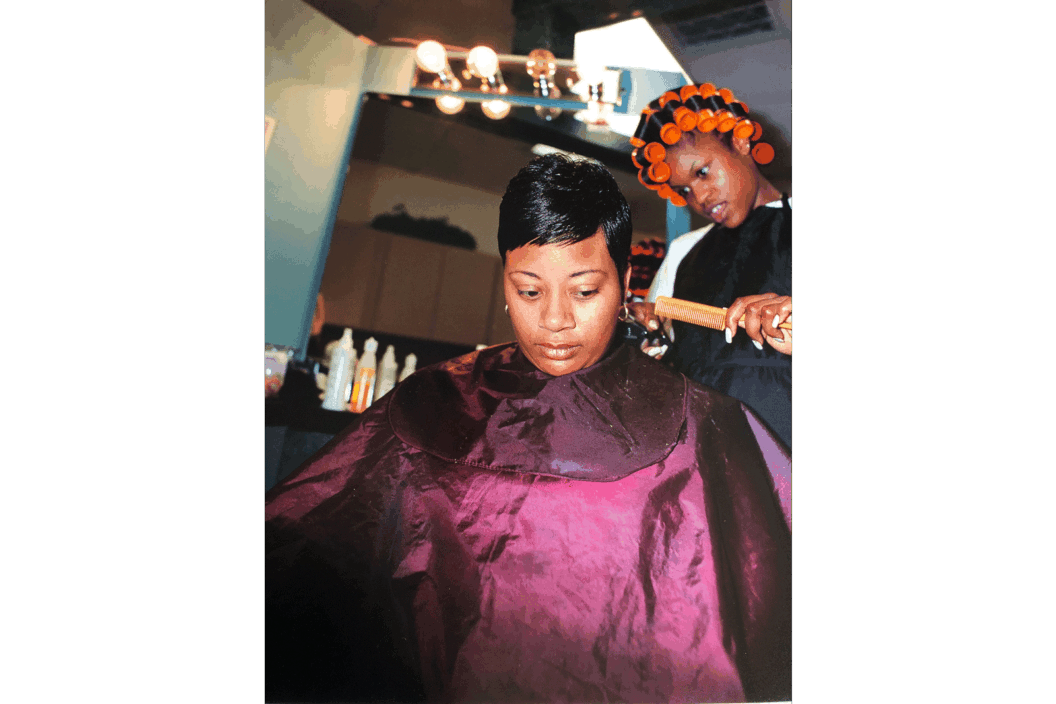 Color photograph of a woman doing the hair of another woman in a purple salon bib.