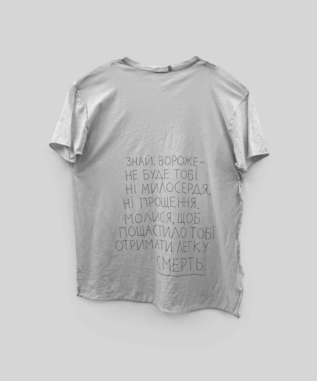 A photograph of a poem-prayer written in black ink on a plain white t-shirt.