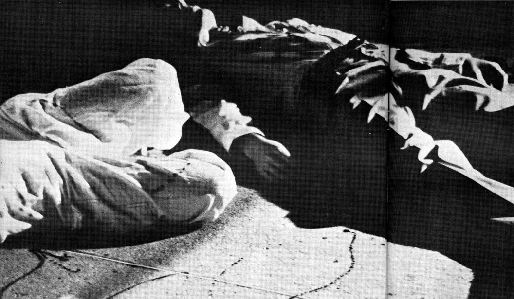 Two people lie on the ground at night in contrasty light. Only the torso of one person and the legs of the other are visible.