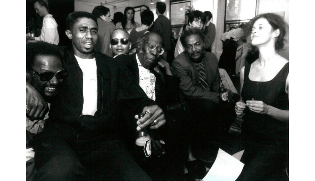 A black and white photograph of Steve Cannon, James Little, Ms. Pryor, Robert Blackburn, John Ferris, and Kiki Nienaber at a party in 1996.