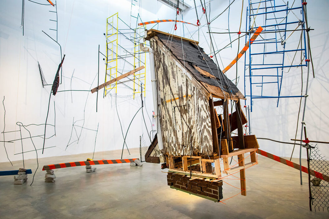 Large sculpture featuring ladders, scaffolding, stones, wire, wood, and fencing titled, Ballast and Barricades, by Michelle Lopez
