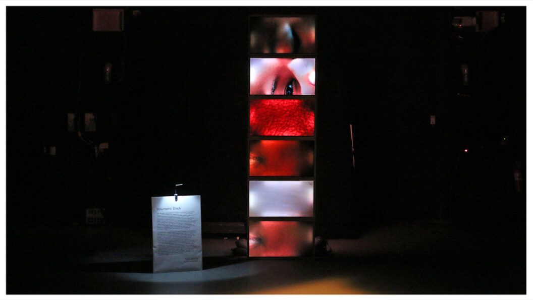 Stacked video screens in a blackened gallery with closeup images of the body: eyes, skin, blood vessels, etc.