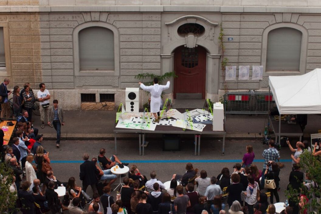 967 Photograph of crowd of people outside watching a person performing on top of a table with paper drawings on it