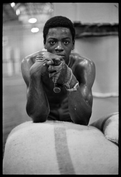 Black-and-white photograph of a Black man looking at the camera, leaning on a sack.