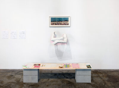 An installation featuring a folded pair of white arms on the wall above a low table with printed materials