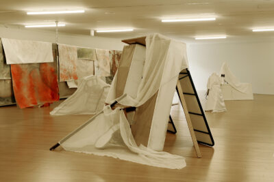 A set of painted canvases and white sheets hang over objects and a long line dividing a large room.