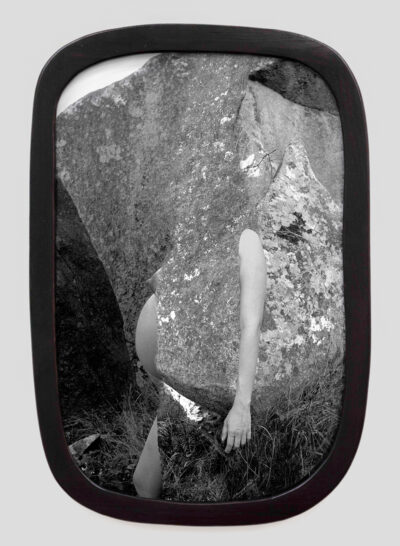 A black-and-white photograph of a figure emerging from large rocks.