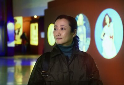 The wife character, played by Zhao Tao, wanders through Torino's cinema museum. Oval images of film stars and scenes are blurred on the background, projected onto oxblood walls.