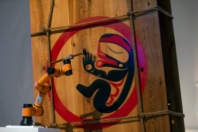 A detail image of an Indigenous ritual figure with a drum mallet next to it.