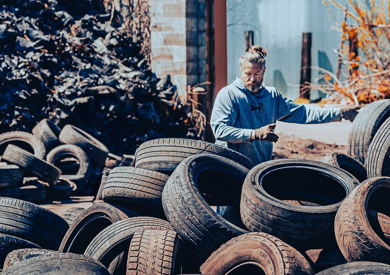 A man is pictured wearing gloves and picking up and sorting used tires for processing.