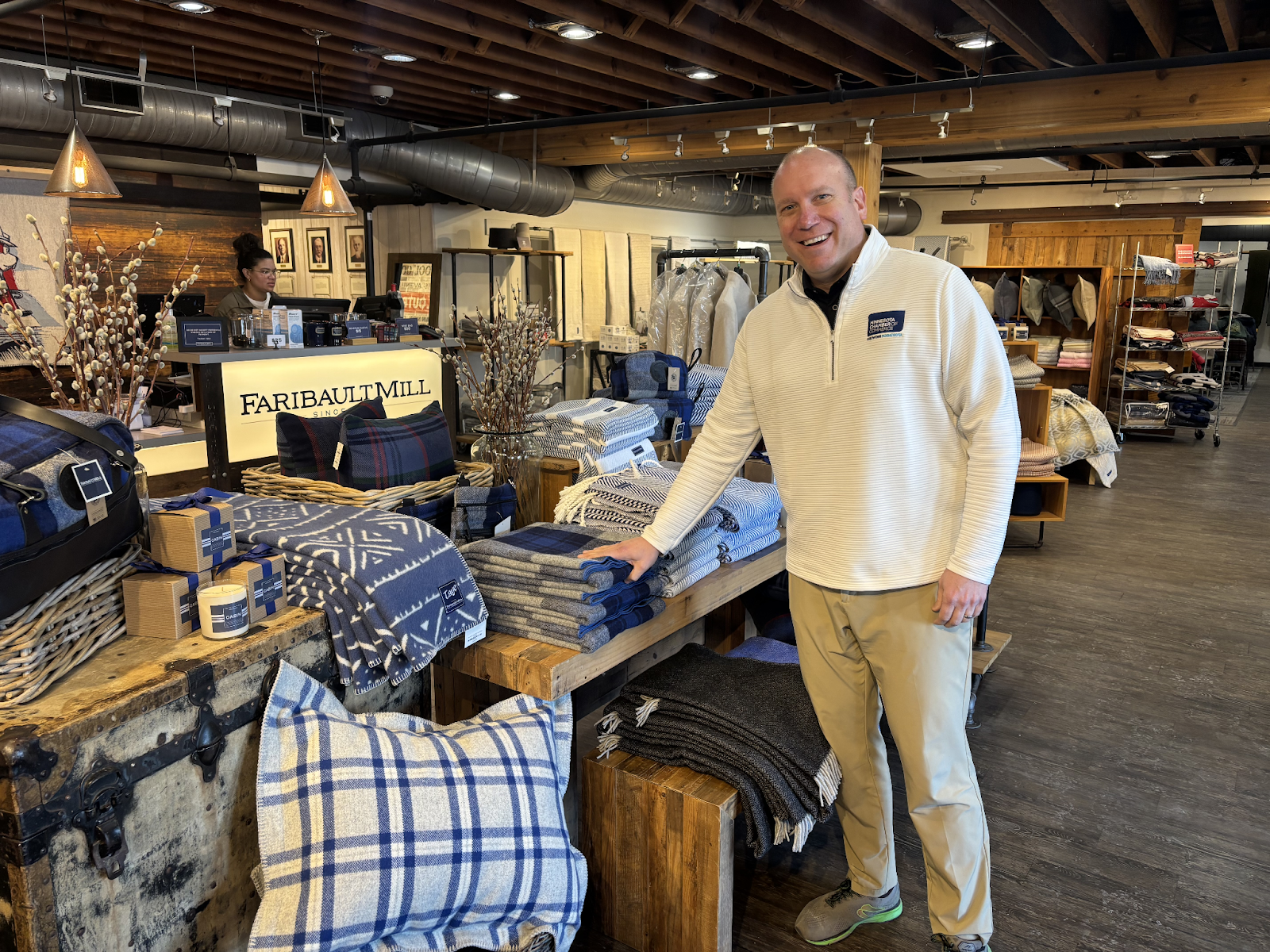 Ross Widmoyer, CEO of Faribault Mills, standing in a Faribault Mills store next to a table covered with merchandise, including hand towels, throw pillows, blankets, and candles.