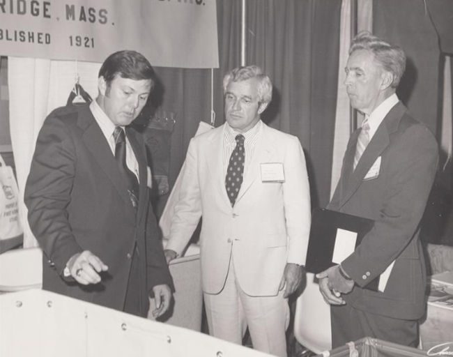 A black-and-white historical photo of the prior management of Steele Canvas pictured in their booth at a trade show.