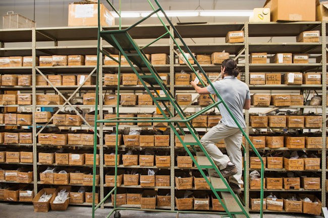 A man climbs a ladder in a warehouse. He is checking an inventory of supplies