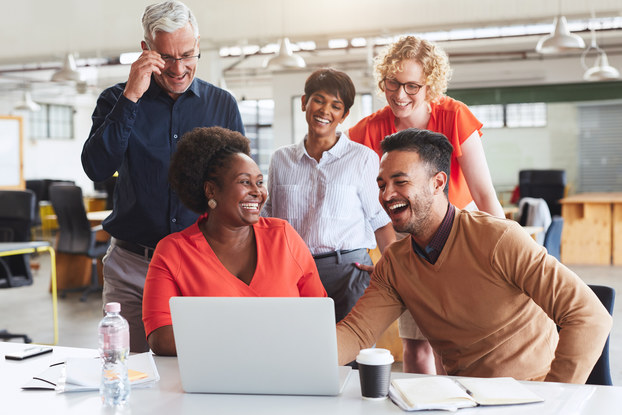 group of happy employees standing around a laptop