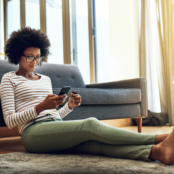 woman sitting on floor in house shopping on her phone