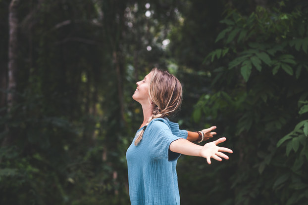 woman standing in nature with her head up and arms out