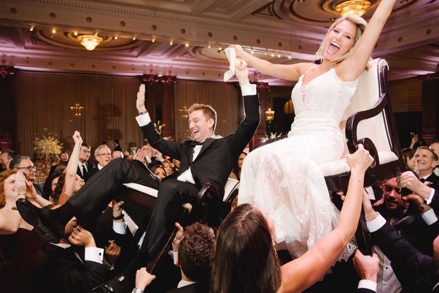 Scene from a wedding with bride and groom lifted in chairs.