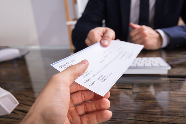 A close-up of two hands reaching across a desk, with one hand giving a check to the other.