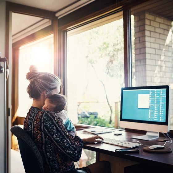 woman holding baby while working at home on laptop