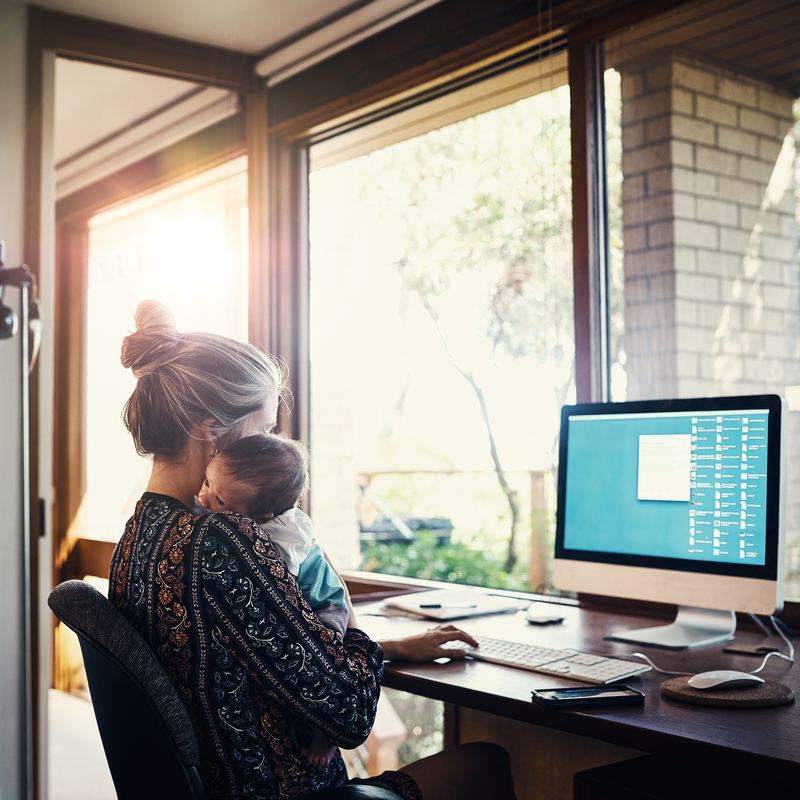 woman holding baby while working at home on laptop