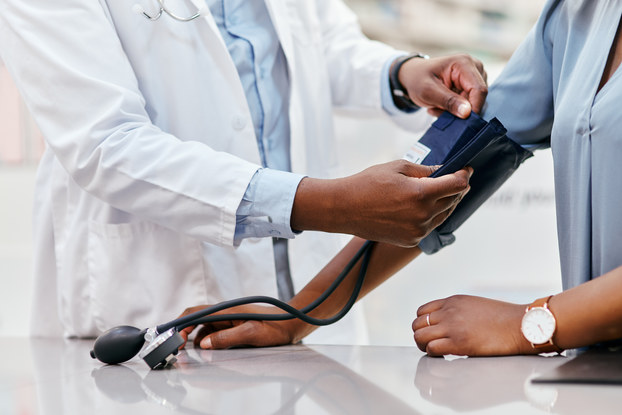 A shoulders-down shot of a doctor in a white lab coat administering a blood pressure test.
