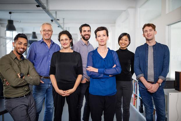 A full shot of a diverse group of seven men and women smiling confidently.